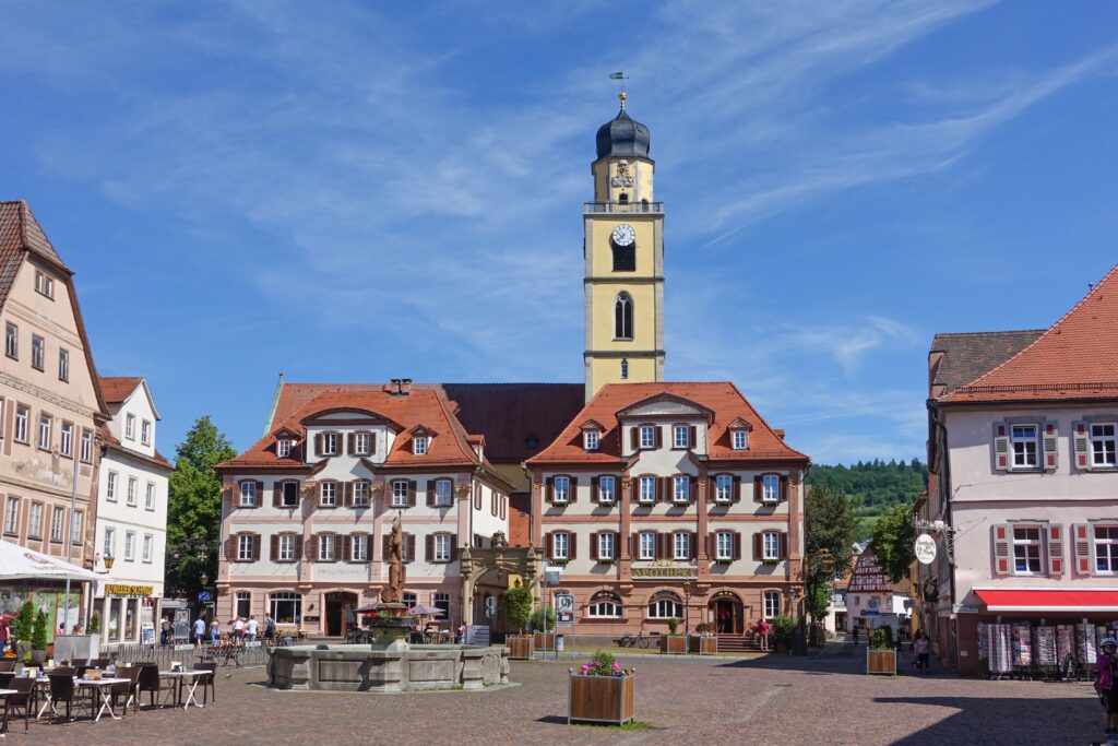 Historic building in a town square with flags and cloudy sky.