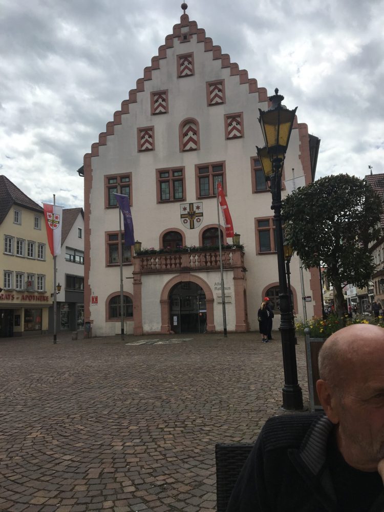 Historic building in a town square with flags and cloudy sky.