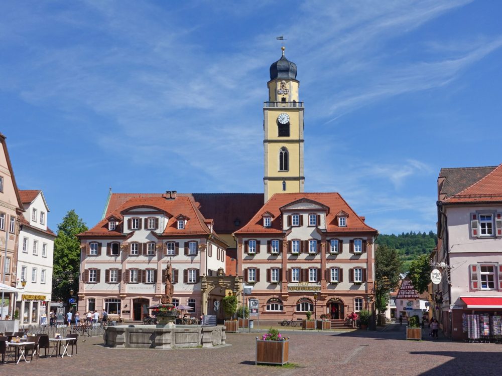 Historic building in a town square with flags and cloudy sky.