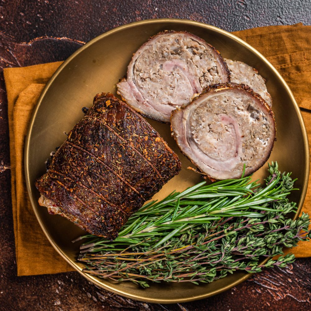 Slices of roasted stuffed pork meat roulade on a plate with ros